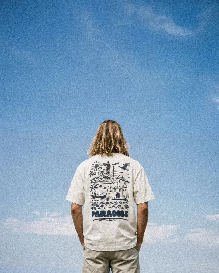 Homem de cabelo longo de costas, camiseta Paradise, céu azul