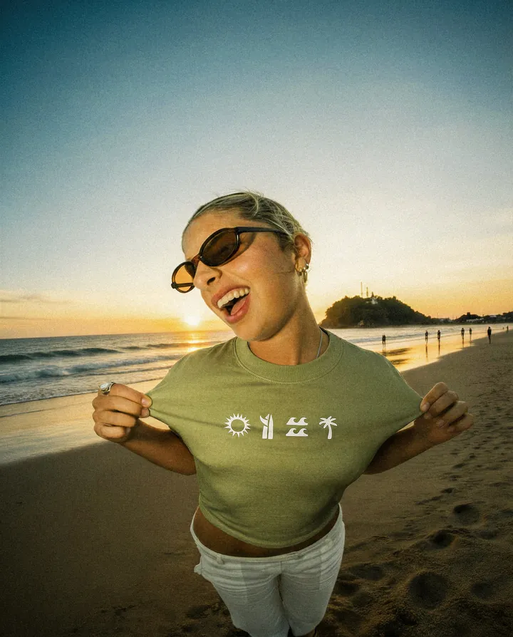 Mulher sorrindo de óculos escuros, camiseta verde Paradise, pôr do sol