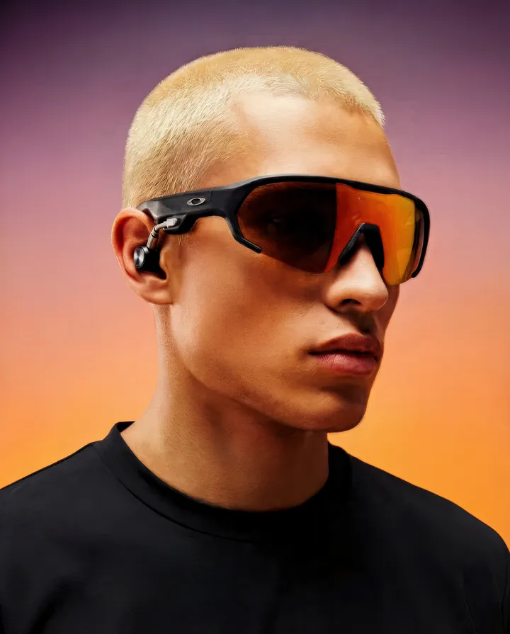 Homem de cabelo platinado de perfil com o óculos, fundo laranja